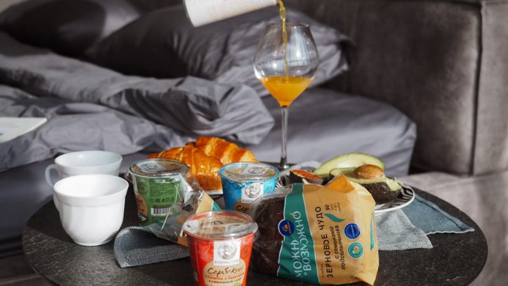 Cozy breakfast setup with croissant, juice, and yogurt on bedside table, creating a relaxing morning vibe.