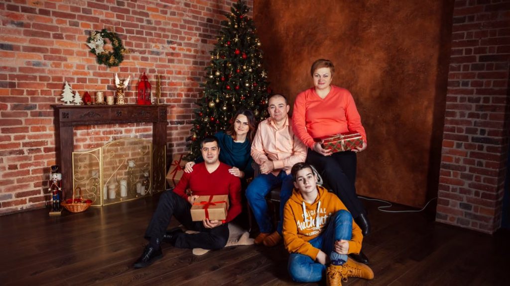 A family posing with Christmas gifts by a decorated tree indoors, exuding holiday warmth.
